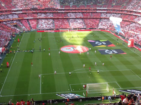 Aerial view of a soccer field during a match in a packed stadium with players and fans.
