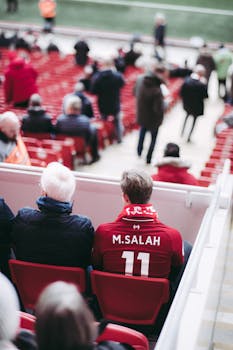 Fans in red jerseys sit in a stadium, showcasing football spirit with vibrant energy.