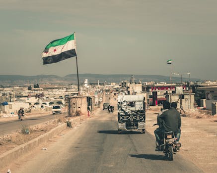 A Middle Eastern town street with a flag, vehicles, and clear sky, capturing a rustic and everyday life vibe.