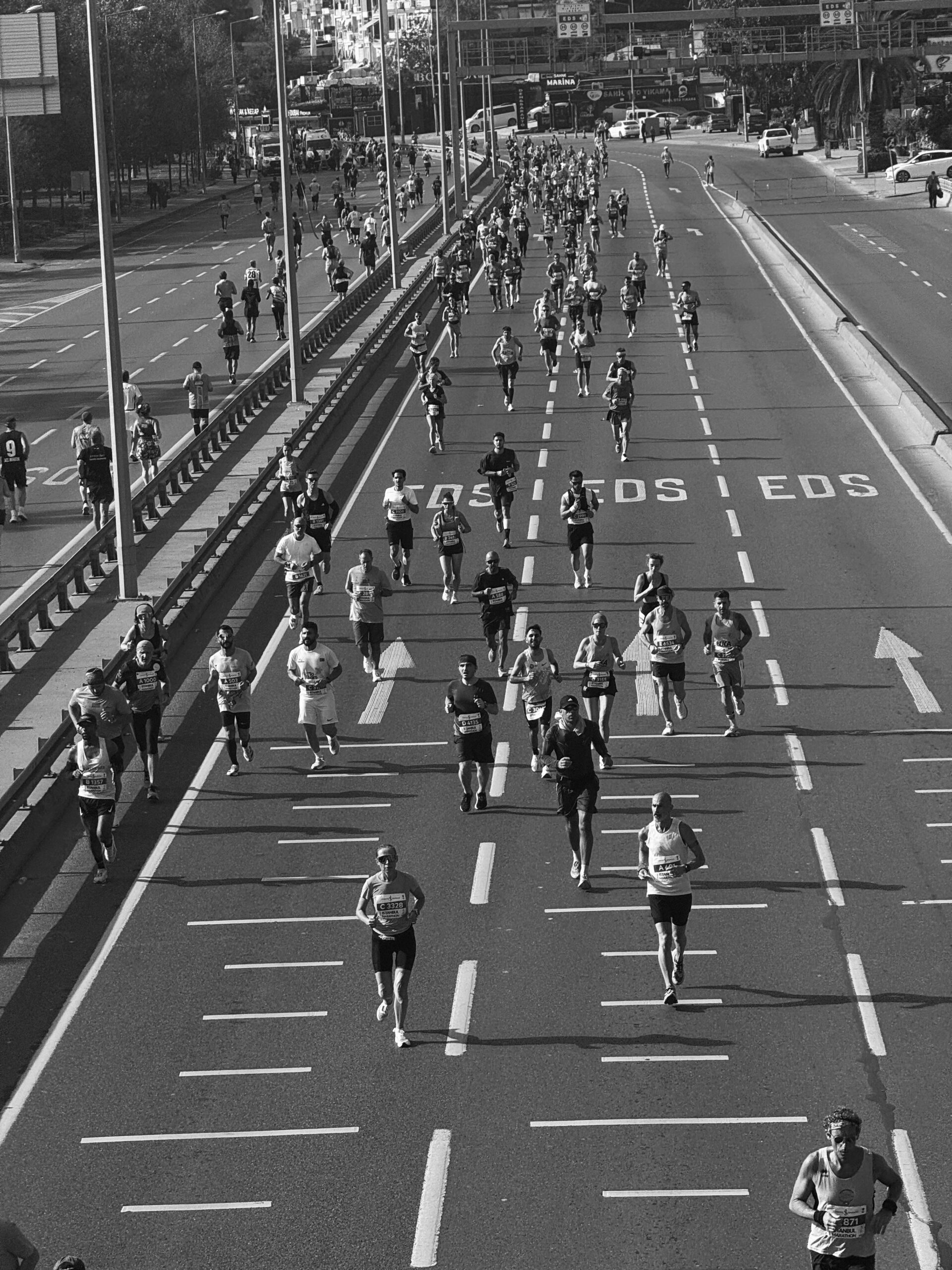Black and white photo of marathon runners on urban road during daytime race.