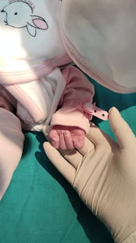 A newborn baby in a cute pink outfit holds a gloved hand, symbolizing care.