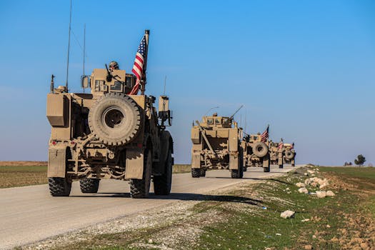 American military convoy driving through rural Syria under a blue sky.