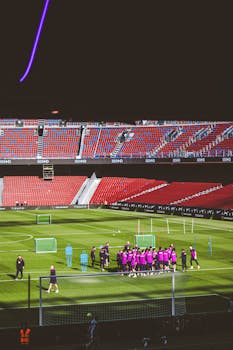 Soccer team practicing on a green field in a large empty stadium, preparing for a match.