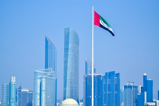 Modern skyline of UAE cityscape with national flag waving against clear sky.