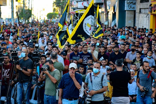 A vibrant demonstration with flags and photographers on a street in Gaza.
