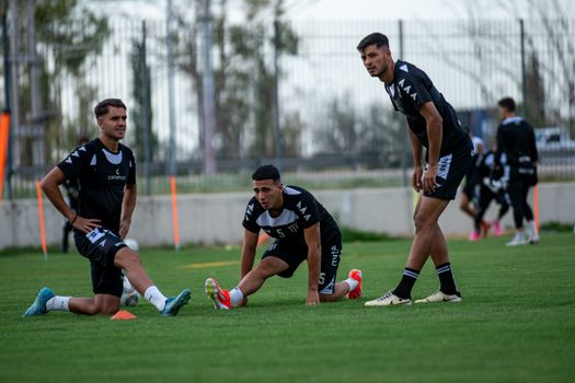 Three male football players stretching during training on a sunny field.