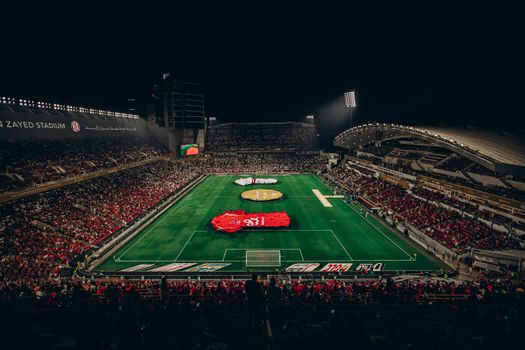 Aerial view of a lively football match at Zayed Stadium, showcasing fans and vibrant atmosphere.
