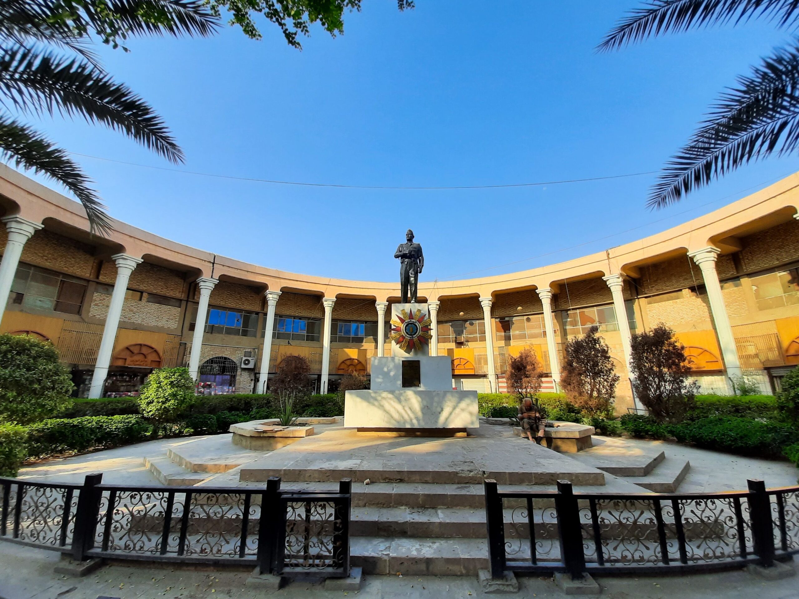 Elegant colonnaded courtyard featuring a prominent statue under a clear blue sky in Baghdad.