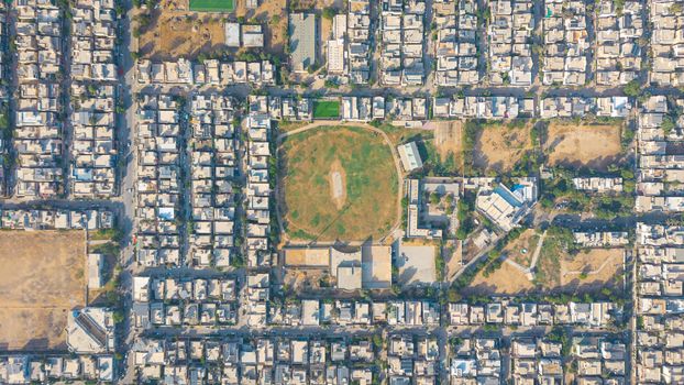 Top-down view of a densely populated neighborhood in Karachi, featuring a cricket ground and geometric street patterns.