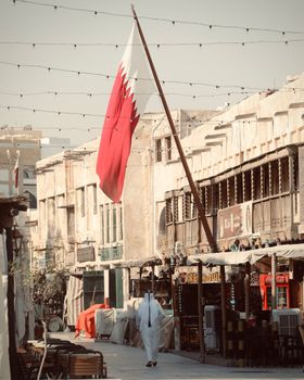 Traditional street in Doha, Qatar with a prominent Qatari flag and local architecture.