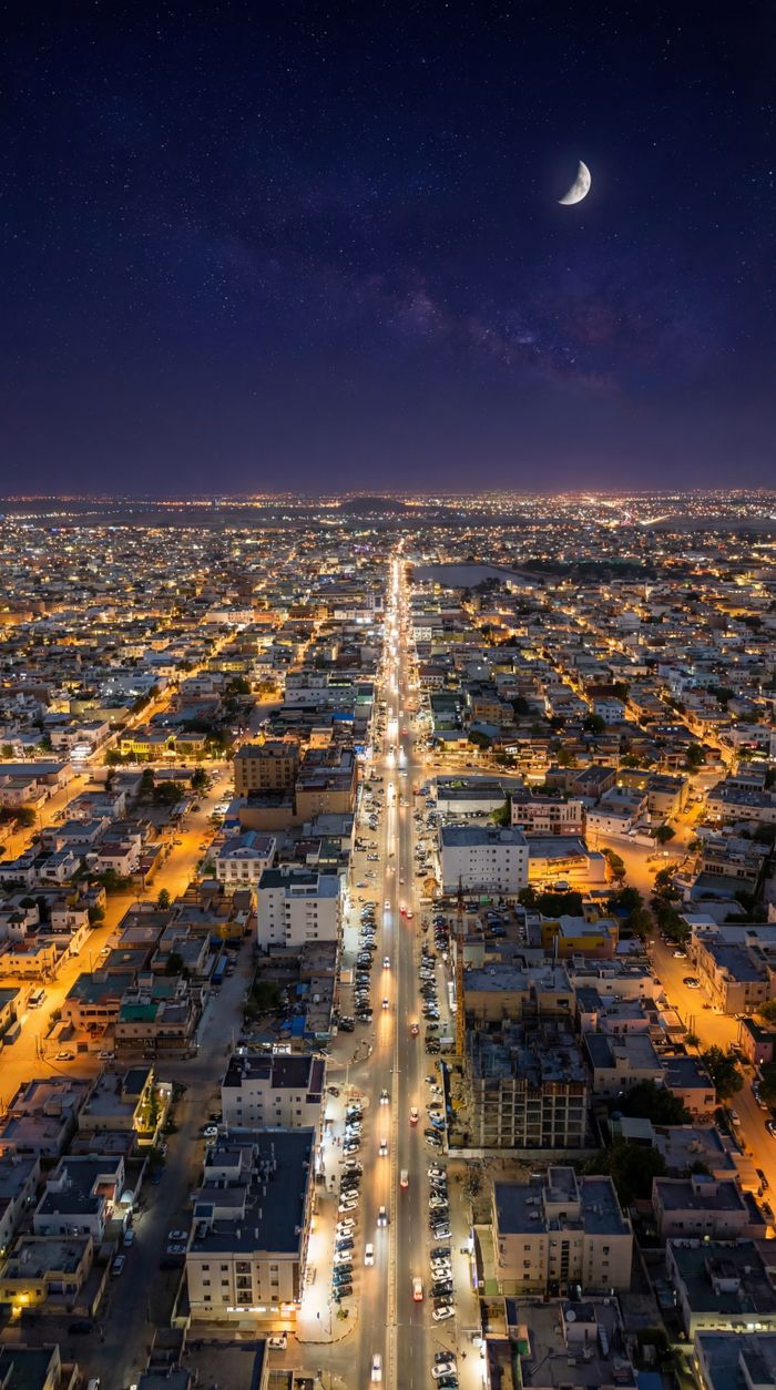 A breathtaking aerial view of a city at night, illuminated by streetlights and a crescent moon.