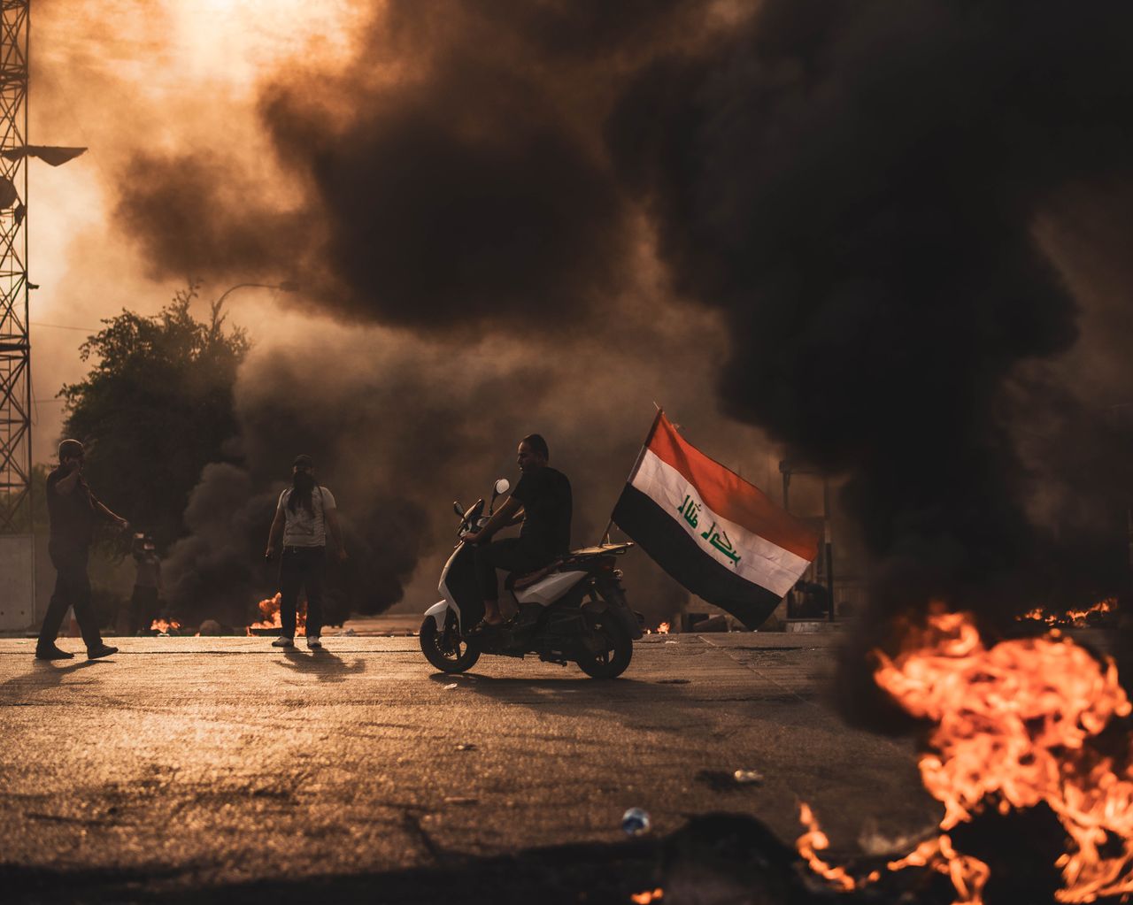 Intense protest scene with people on motorbikes, smoke, and flames, showcasing civil unrest.