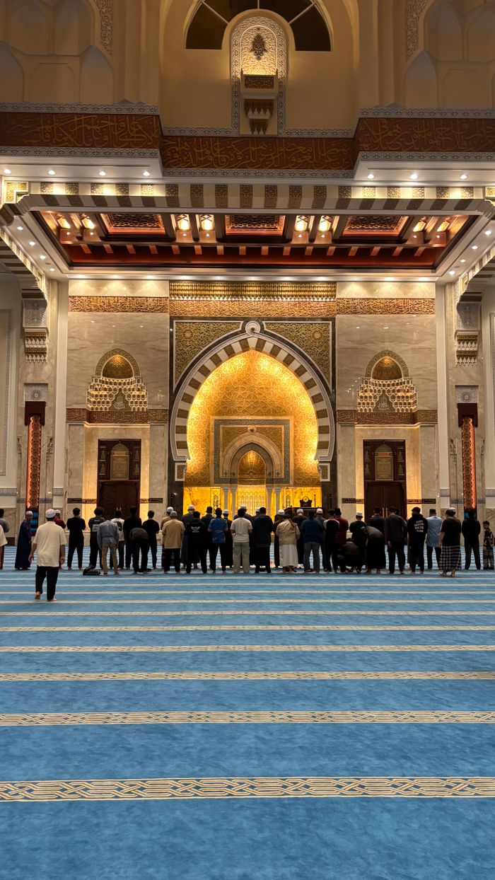 A group of people standing in a beautifully lit grand mosque interior.