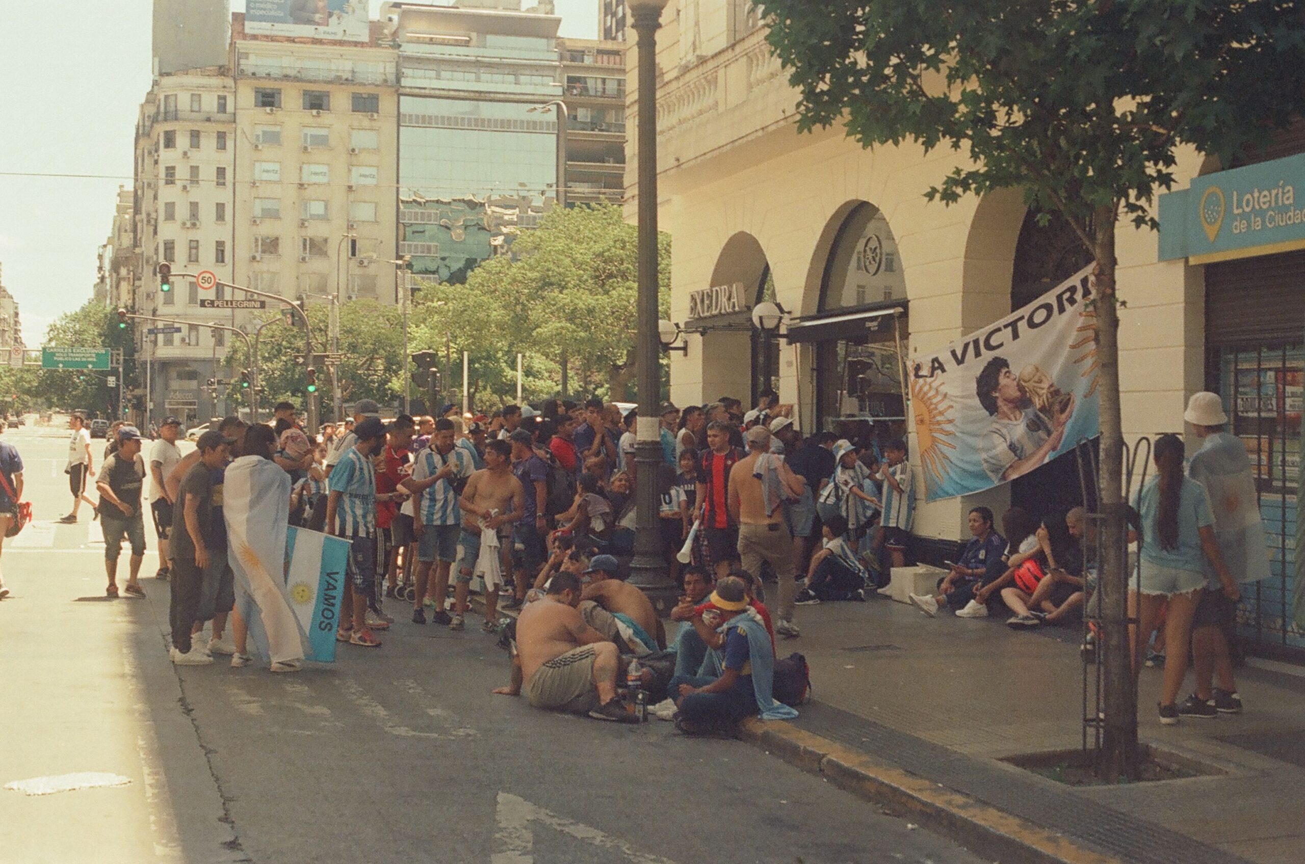 Lively crowd gathers on a bustling street in Buenos Aires, celebrating with flags and banners.